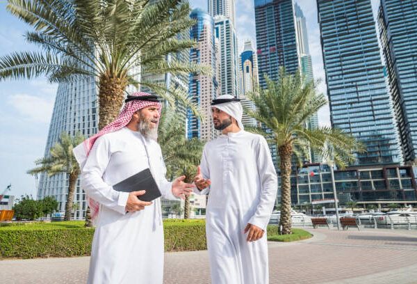 Two businessmen with traditional emirates clothes meeting in Dubai - Senior and young adults having business in the UAE