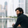 Young man with beard standing outside. He is wearing black shirt and looking at the view and smile